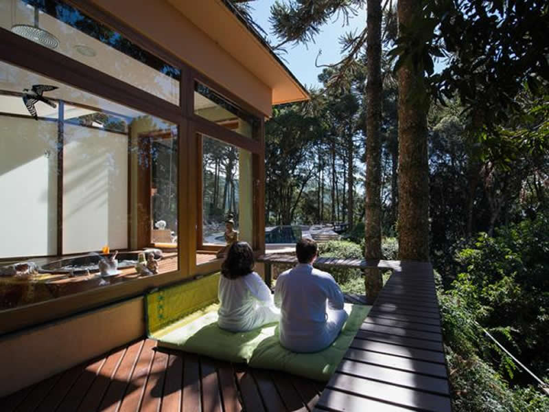 Casal de roupão no deck de uma morada contemplando a mata de araucárias ao lado do ofurô