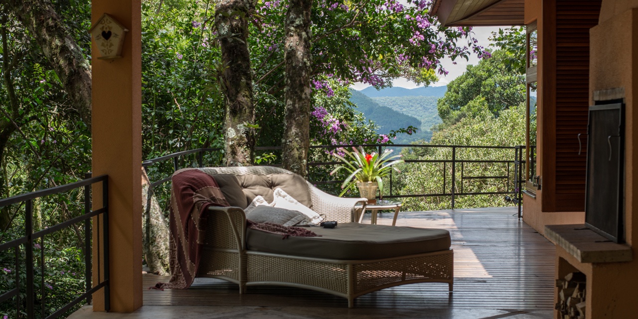 Deck privativo com espreguiçadeira e vista panorâmica das montanhas, entre buganvílias